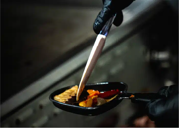 Photo prise lors d'un tournage d'une publicité pour un restaurant. On y voit la main d'un chef faisant cuire du fromage et des légumes dans une raclette.