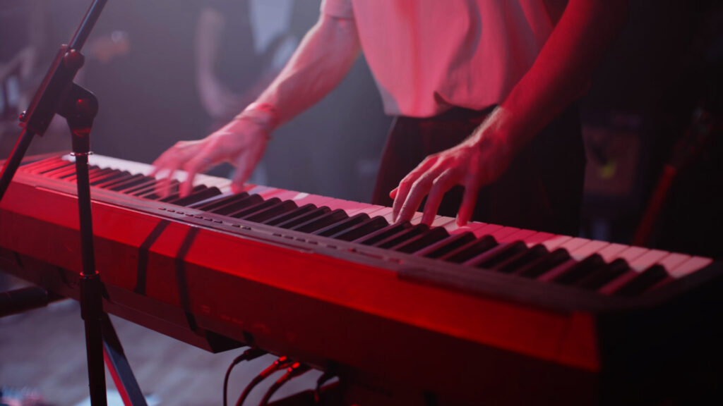 Le chanteur et musicien Thomas du groupe Alabel au clavier en plan serré lors d'une prestation de concert filmé en multicaméras par la Mine productions