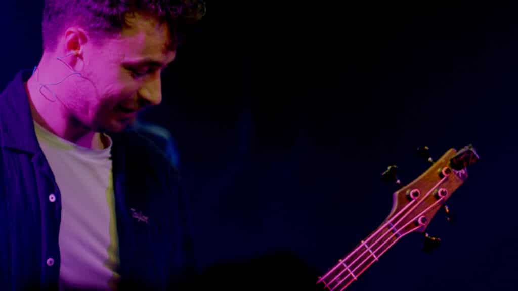 Le guitariste du groupe Alabel debout sur scène devant son micro lors d'une prestation de concert filmé en multicaméras par la Mine productions
