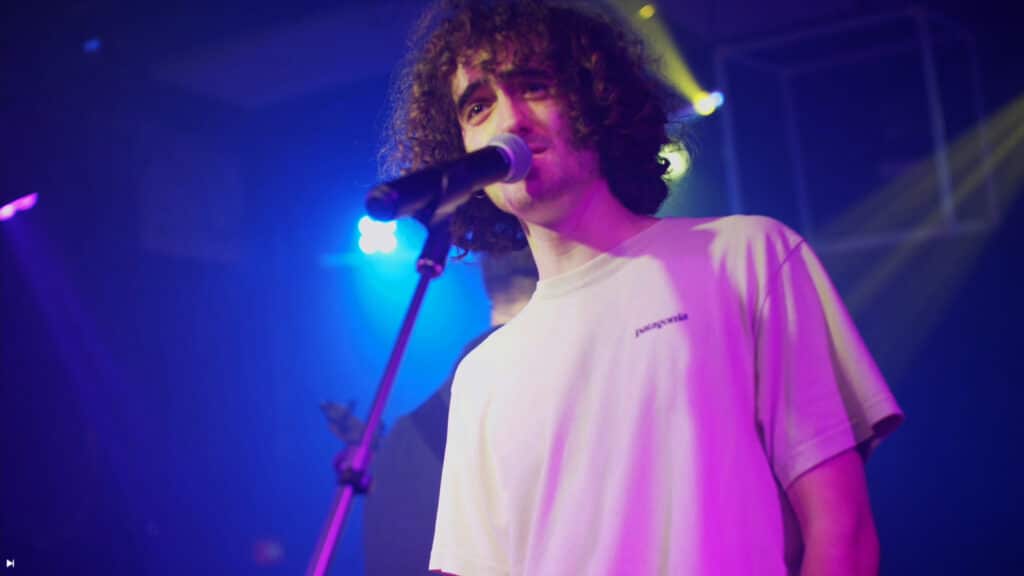 Le chanteur et musicien Thomas du groupe Alabel debout sur scène devant son micro lors d'une prestation de concert filmé en multicaméras par la Mine productions