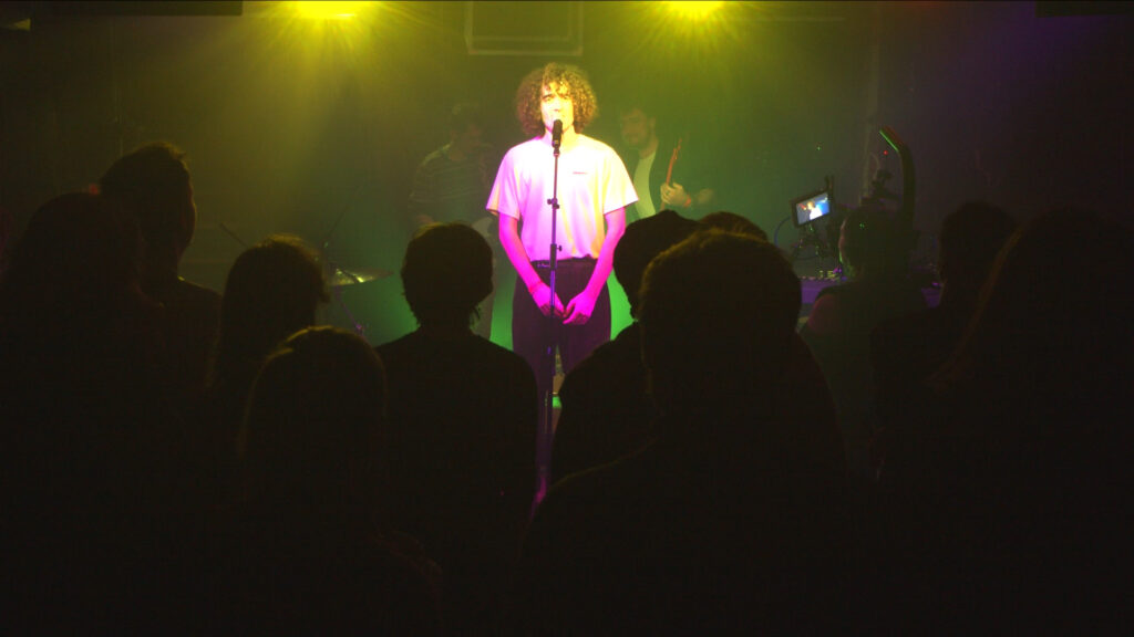 Le chanteur et musicien Thomas du groupe Alabel debout sur scène devant son public lors d'une prestation de concert filmé en multicaméras par la Mine productions
